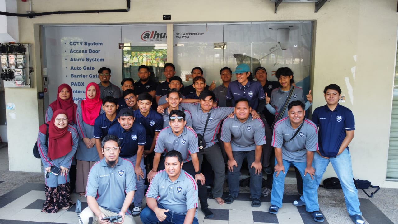 Zashtech team group photo outside the office, standing in front of Dahua Technology Malaysia signage listing CCTV, Access Door, Alarm System, Auto Gate, Barrier Gate, PABX, Intercom and Network services